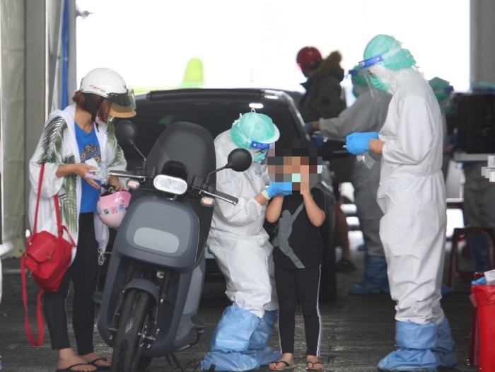 本土疫情升溫，一位家長帶著小孩騎車前往排隊篩檢。（張鎧乙攝）