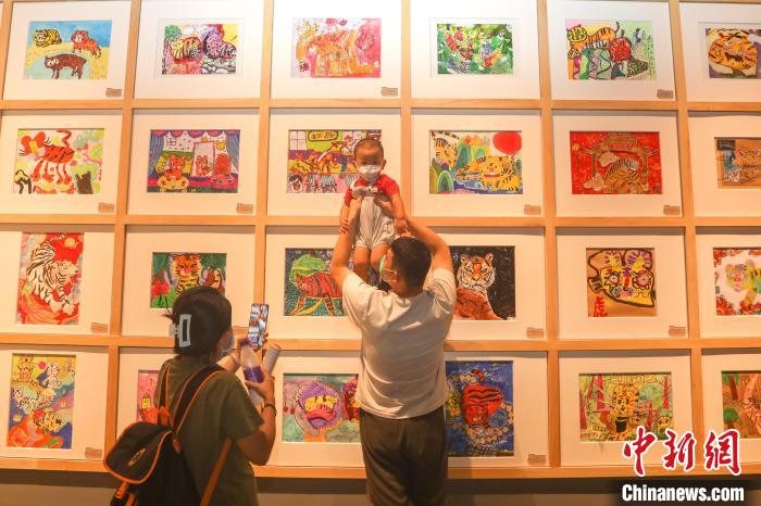 图为一位家长带着小朋友在展出的老虎主题儿童艺术作品前拍照。　刘力鑫 摄