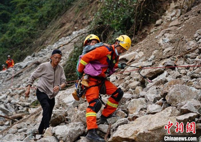 救援人员背着孩子通过山体垮塌危险地带。　四川应急供图