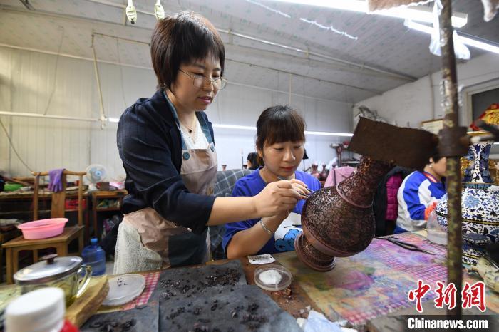 圖為河北省巧手脫貧示範基地總工藝師王靜正在指導女工為景泰藍工藝品“掐絲”。