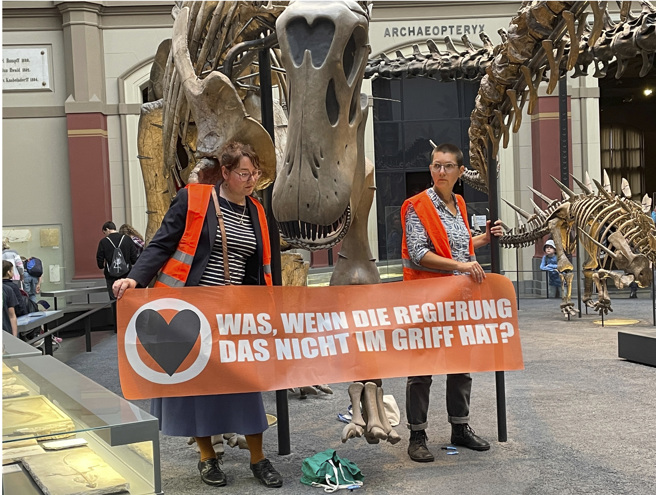 德国环保组织成员将自己粘在恐龙骨架下抗议。（图源：美联社）