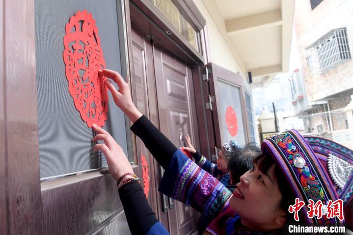 图为仫佬族剪纸艺人给农户大门贴上“生肖兔”剪纸作品。　廖光福 摄