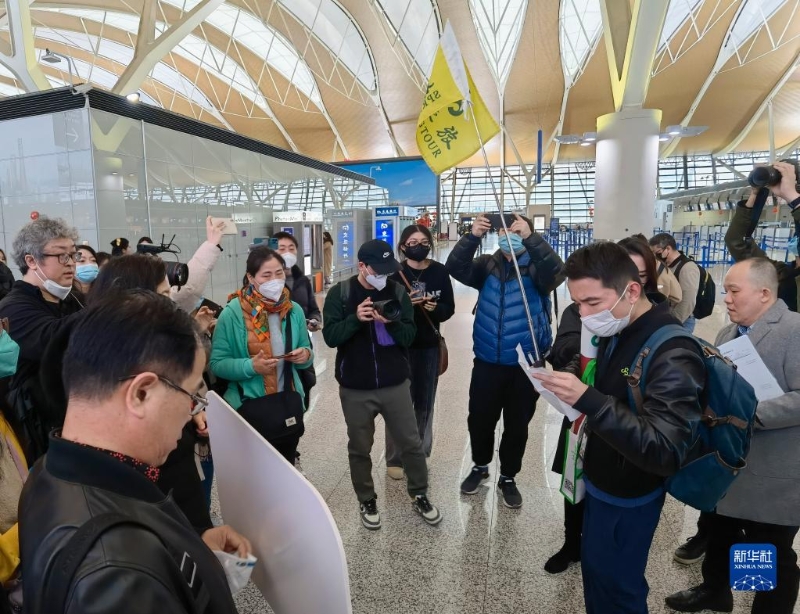 2月6日，在上海浦东国际机场，出境团队游领队师文（举旗者）向游客说明相关注意事项。（图源：新华社）