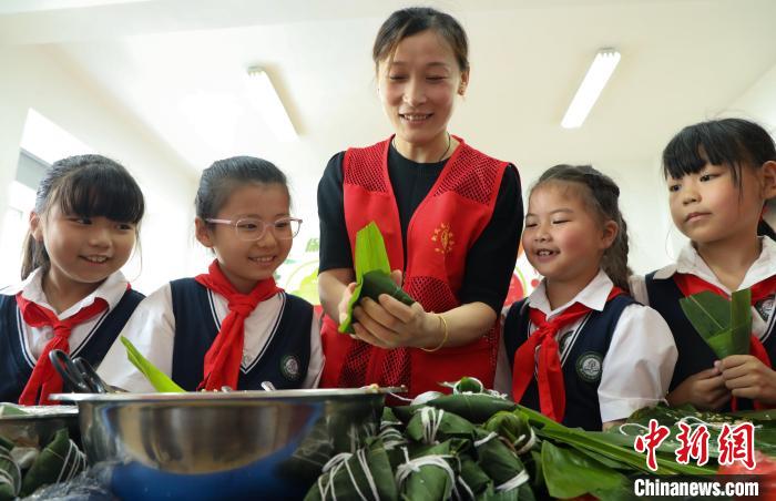安徽省肥西县上派镇四十埠社区志愿者教小学生们包粽子。　陈家乐 摄