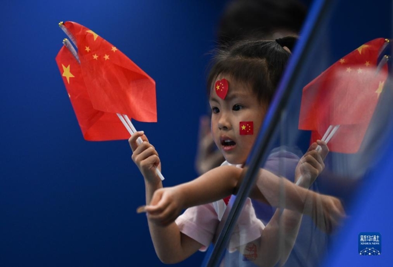 9月25日， 一名小观众在看台上挥舞国旗。当日，杭州亚运会游泳比赛在浙江杭州奥体中心游泳馆继续进行。（图源：新华社）